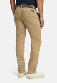 Chino beige a taglio slim, con tasche posteriori e cintura blu navy texturizzata. Indossati con sneakers bianche, per un look casual.