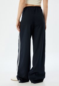 Marineblauwe wijde broek met een elastische tailleband, voorzien van witte zijstrepen. Gemaakt van zachte stof, hebben ze een gladde textuur en een comfortabele pasvorm.