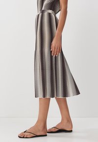 Abito a strisce nero e crema con orlo svasato, texture a coste e corpetto aderente. Abbinato a sandali flip-flop neri minimalisti.