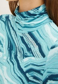 Maglione a collo alto turchese con un motivo astratto ondulato in accenti blu scuro e bianco, realizzato in un tessuto morbido e elasticizzato.