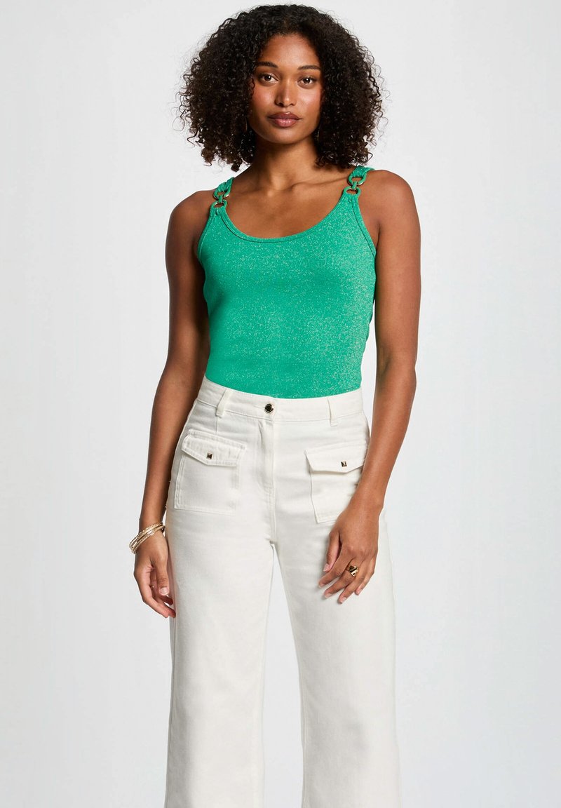 Groene glitter tanktop met decoratieve schouderhardware, gecombineerd met hoge taille witte wijde broek met voorzakken.