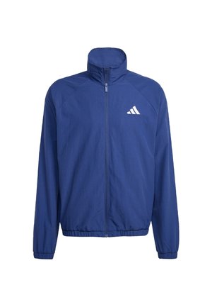 Navyblå zip-up jacka med hög krage, elastiska mudd och fåll. Har en vit logotyp på vänster bröst och är tillverkad av ett slätt, lätt tyg.