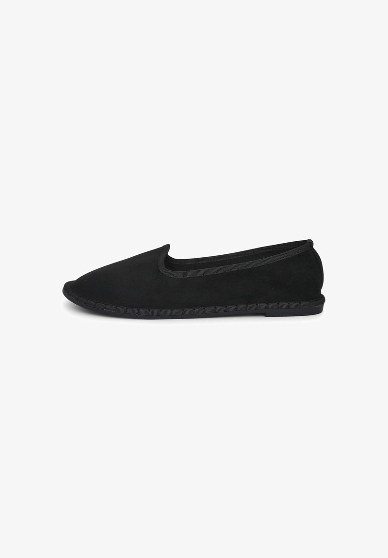 Chaussure slip-on en suede noire avec un orteil arrondi, un bord élastique et une semelle texturée, présentant un détail tressé le long du bord.