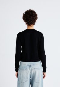 Zwarte gebreide trui met lange mouwen, ronde hals en een gladde textuur, gecombineerd met lichtblauwe hoge taille denim jeans.