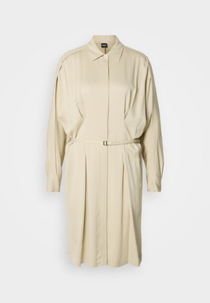 Béžové šaty košeľového strihu s dlhými rukávmi, golierom, zapínaním na gombíky, záhybmi a tenkým opaskom v páse na jednotnom pozadí.