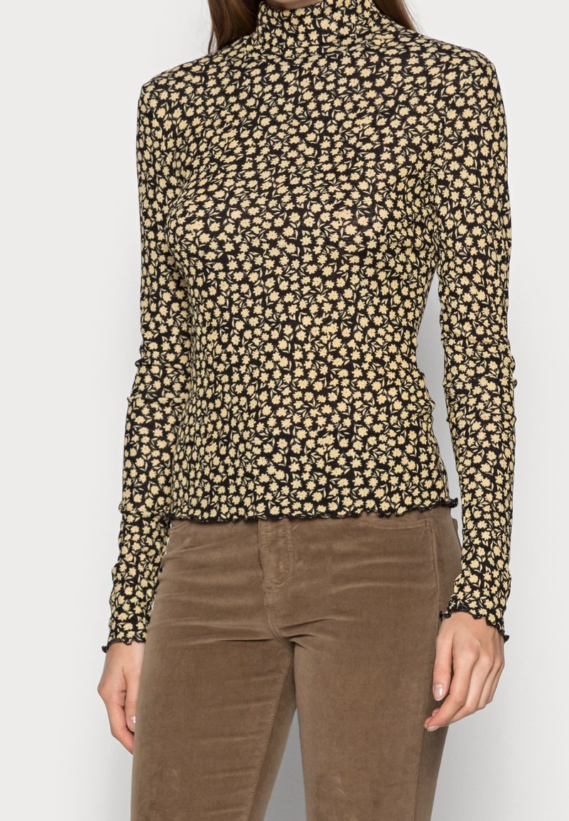Mouwenlange turtleneck top in zwart met een gele bloemenprint, met een getailleerd ontwerp en een geschulpte zoomafwerking.
