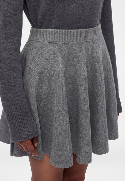 Gros plan d’une personne portant une jupe évasée en maille grise et un pull à manches longues assorti avec des poignets côtelés.