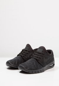 Chaussures de sport noires avec une tige en mesh texturé, une silhouette élégante, un bout rond et une semelle rembourrée comprenant une unité d'air visible et des lacets.