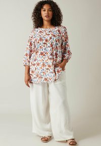 Bluse med blomsterprint og trekvartærmer i hvid, orange og blå. Sammen med brede hvide bukser og brune sandaler.