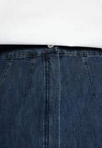 Tmavě modré denimové džínsy s elegantním designem, které mají zapínání na knoflík a vertikální švy. Textura je měkká s mírným vyblednutím.