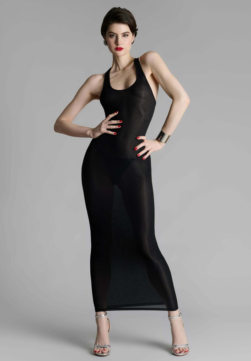 Robe maxi noire transparente avec un design dos nageur, présentant une silhouette ajustée et une texture lisse, associée à des sandales à talons hauts argentées.
