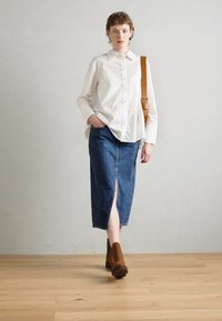Hvit skjorte med knapper, denim midi-skjørt med frontsplitt og brune ankelstøvler. Minimalistisk design mot en nøytral bakgrunn.