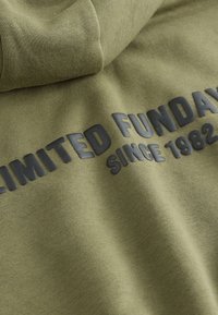 Sweat à capuche vert olive avec une texture douce. Présente un texte graphique noir audacieux indiquant "LIMITED FUNDAY depuis 1982" sur le devant.