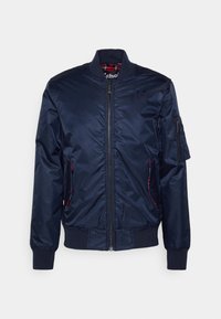 Námořnická modrá bomber bunda s předním zipem, žebrovaným límcem, manžetami a spodním lemem, kapsou na zip na rukávu a bočními kapsami se zavíráním na patent.