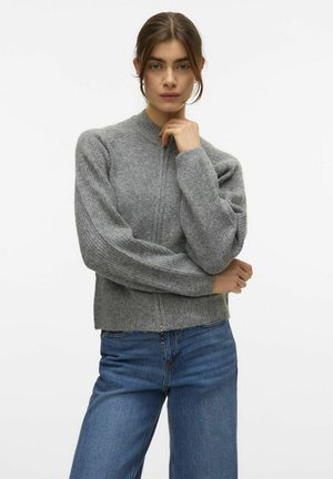 Grå strikket sweater med høj krave og ribbede ærmer, med lynlås og en afslappet pasform, parret med blå jeans.