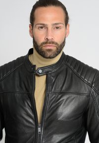 Sort læderjakke med høj krave, med quiltede skulderdetaljer og lynlås foran, lagdelt over en beige turtleneck.