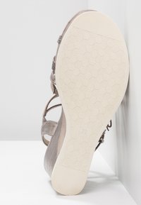 Sandale avec semelle beige texturée, motif géométrique de la bande de roulement, talon compensé et brides en tissu gris, vue par dessous. Taille 37 indiquée sur la semelle.