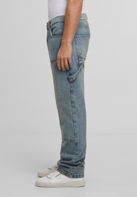 Hellblaue Denim-Jeans mit geradem Bein, ausgestattet mit Seitentaschen und einem klassischen Knopfverschluss. Getragen mit weißen Sneakers.