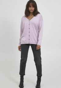 Hellblaues Button-Up-K cardigan mit V-Ausschnitt, langen Ärmeln und einer lockeren Passform. Kombiniert mit dunkelgrauen Jeans und schwarzen Stiefeletten.