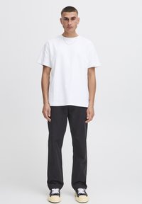 White cotton t-shirt with short sleeves, relaxed fit, and a crew neck; paired with black trousers and black and white sneakers.