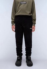 Črne športne hlače z elastiko v pasu, stranskimi žepi in detajlom z logotipom. Kombinirane z olivno zeleno majico z dolgimi rokavi.