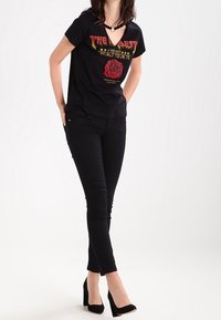 Svart T-shirt med röd och gul grafisk tryck som säger "HJÄRTAT" och rosdesign. I kombination med svarta skinny jeans och svarta klackar.