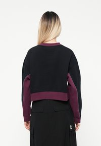 Kuttet sweatshirt med svart kropp og lilla detaljer på ermene og kragen. Laget av myk stoff med ribbestrikkede mansjetter og kant.
