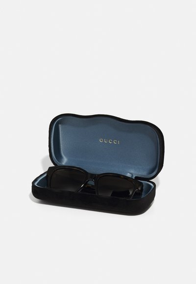 Ochelari de soare Gucci negri într-un etui moale negru cu interior albastru, având un logo aurit în interiorul capacului.