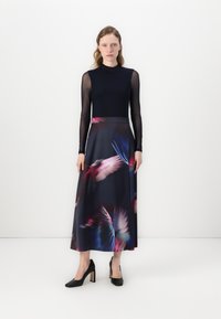 Robe longue avec une base sombre ornée d'imprimés de plumes colorées. Le haut est ajusté avec de longues manches transparentes et un col haut.