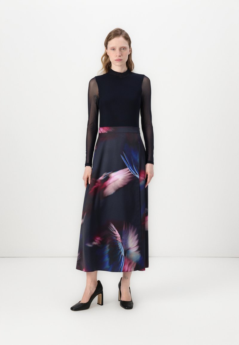 Robe longue avec une base sombre ornée d'imprimés de plumes colorées. Le haut est ajusté avec de longues manches transparentes et un col haut.