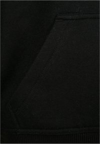 Gros plan d'une poche en tissu noir avec des coutures visibles sur un vêtement, montrant la texture et les détails des coutures.