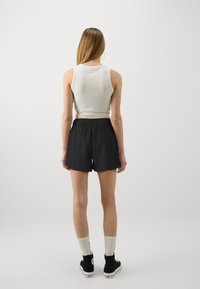 Top fără mâneci alb, ajustat, și pantaloni scurți negri cu talie elastică. Adidași negri înalți cu talpa albă și șosete albe de mijloc cu logo.