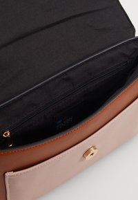 Beige ja vaaleanpunainen käsilaukku, jossa on sileä pinta, kultaiset yksityiskohdat ja vetoketjupussi sisällä, musta vuori.