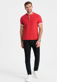 Rød polo shirt med hvide accenter, korte ærmer og tre-knaps lukning. Sammen med sorte bukser og hvide sneakers. Enkel og moderne design.