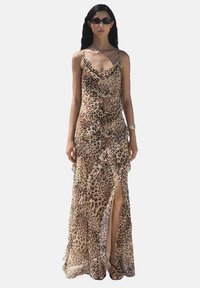Abito maxi a stampa leopardata con design arricciato, tessuto trasparente e uno spacco fino alla coscia; accessoriato con occhiali da sole e un bracciale.