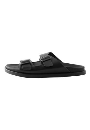 Sandalia tipo slide negra con dos correas ajustables y hebillas, suela plana y diseño de dedo abierto.