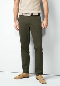 Olivgrüne karierte Hose mit schlankem Schnitt, kombiniert mit einem gewebten beigen Gürtel und hellbraunen Loafers. Glatte Textur mit dezentem Muster.