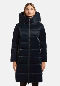 Parka imbottita blu navy con colletto alto, zip a tutta lunghezza e motivo trapuntato orizzontale. Presenta tasche laterali e una texture lucida.
