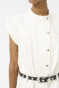 Robe sans manches en denim blanc avec des boutons à l'avant, des coutures orange contrastantes et une ceinture en cuir noir ornée de clous en argent et d'une boucle en métal.
