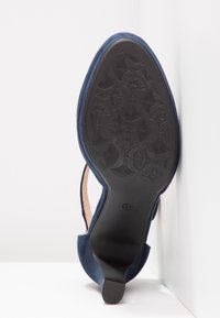 Chaussure à talon pour femme bleu marine positionnée verticalement montrant une semelle noire avec des motifs floraux et en forme d’éventail, taille 37 marquée sur la semelle.