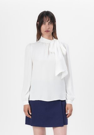 Hvit langermet bluse med høy hals og en stor sløyfedetalj, parret med et mørkeblått skjørt. Glatt stoff og avslappet passform.