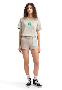 Lichtgrijze t-shirt met een kleurrafische afbeelding en symbolen, gecombineerd met beige high-waisted shorts met een muntgroene zakaccent.