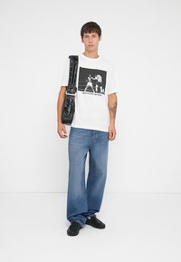 White t-shirt with graphic design featuring boxers, paired with light blue wide-leg jeans and black sneakers, and a black shoulder bag.