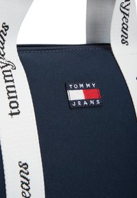 Τσάντα ώμου από ύφασμα σε ναυτικό μπλε με λευκές λαβές και το κείμενο "TOMMY JEANS". Περιλαμβάνει μικρό λογότυπο της μάρκας σε χρώματα κόκκινο, άσπρο και μπλε.
