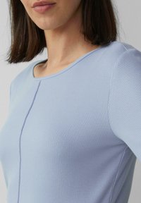 Jasnoniebieski prążkowany top z okrągłym dekoltem i krótkimi rękawami. Materiał ma delikatne pionowe linie i subtelną teksturę.