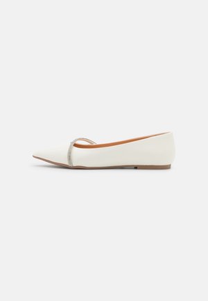 Chaussure plate blanche à bout pointu avec une bride argentée pailletée sur le dessus et une semelle marron.