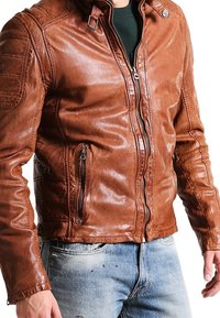Giacca di pelle marrone con un design aderente, chiusura con zip, tasche laterali e dettagli sulle spalle. Tessuto liscio, finitura leggermente usurata.