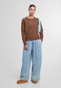 Brauner Pullover mit einem gerippten Saum, hellblaue weit geschnittene Jeans und braune Schuhe. Das Outfit vereint weiche Texturen und kontrastierende Farben.