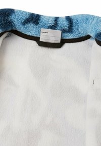 Białe odzienie z polaru wewnątrz z niebieskim kołnierzem w stylu tie-dye. Posiada metkę z napisem "Byłem tutaj" oraz czarne wykończenie wokół kołnierza.