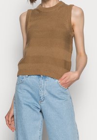 Top sans manches en tricot marron avec une texture côtelée et des rayures horizontales, associé à un jean taille haute bleu clair.